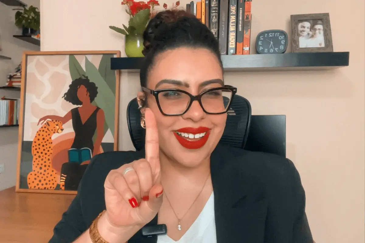 Barbara Rodrigues, especialista em liderança feminina, sorrindo com postura confiante e vestindo um blazer preto. Ao fundo, uma estante com livros e um quadro artístico. A imagem transmite autoridade e autenticidade na liderança.